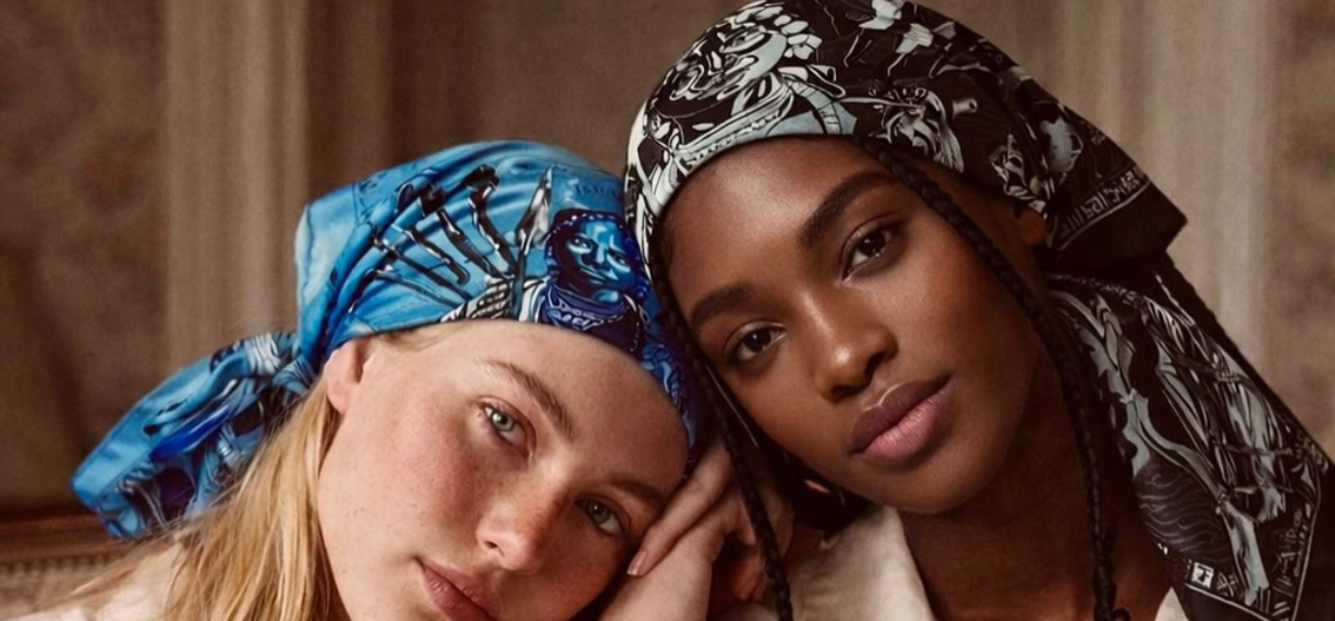 Deux femmes sont assises l'une près de l'autre, chacune portant un foulard à motifs - l'une bleue et l'autre noire et blanche - sur un fond intérieur neutre.