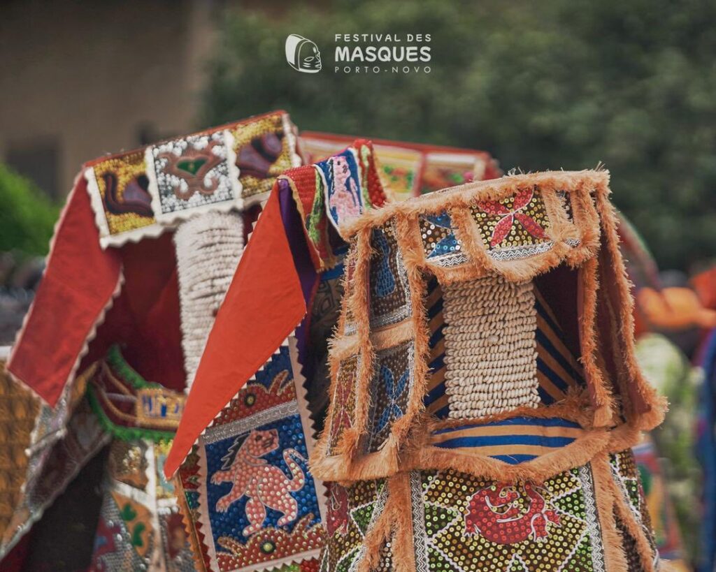 Plusieurs masques colorés et décorés de façon complexe sont portés par des participants au Festival des Masques à Porto-Novo. Les masques présentent des motifs et des textures élaborés.